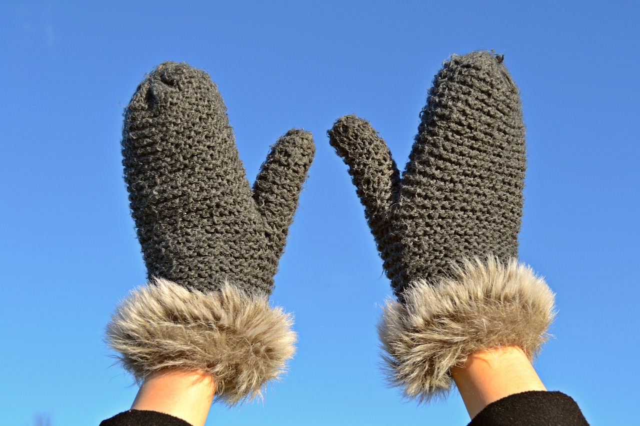 Paire de moufles en laine tricotée tenue à bout de bras sous un ciel d'hiver